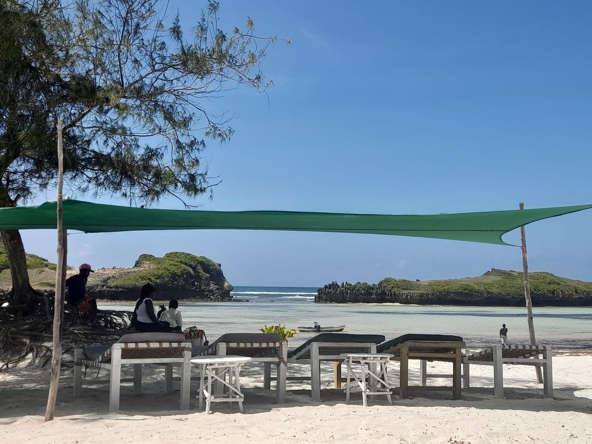 Sunbeds under a shade sail at Ocean Breeze Beach, Watamu, with rocky islets offshore